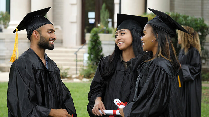 Female college students talk with their male friend after the graduation ceremony.