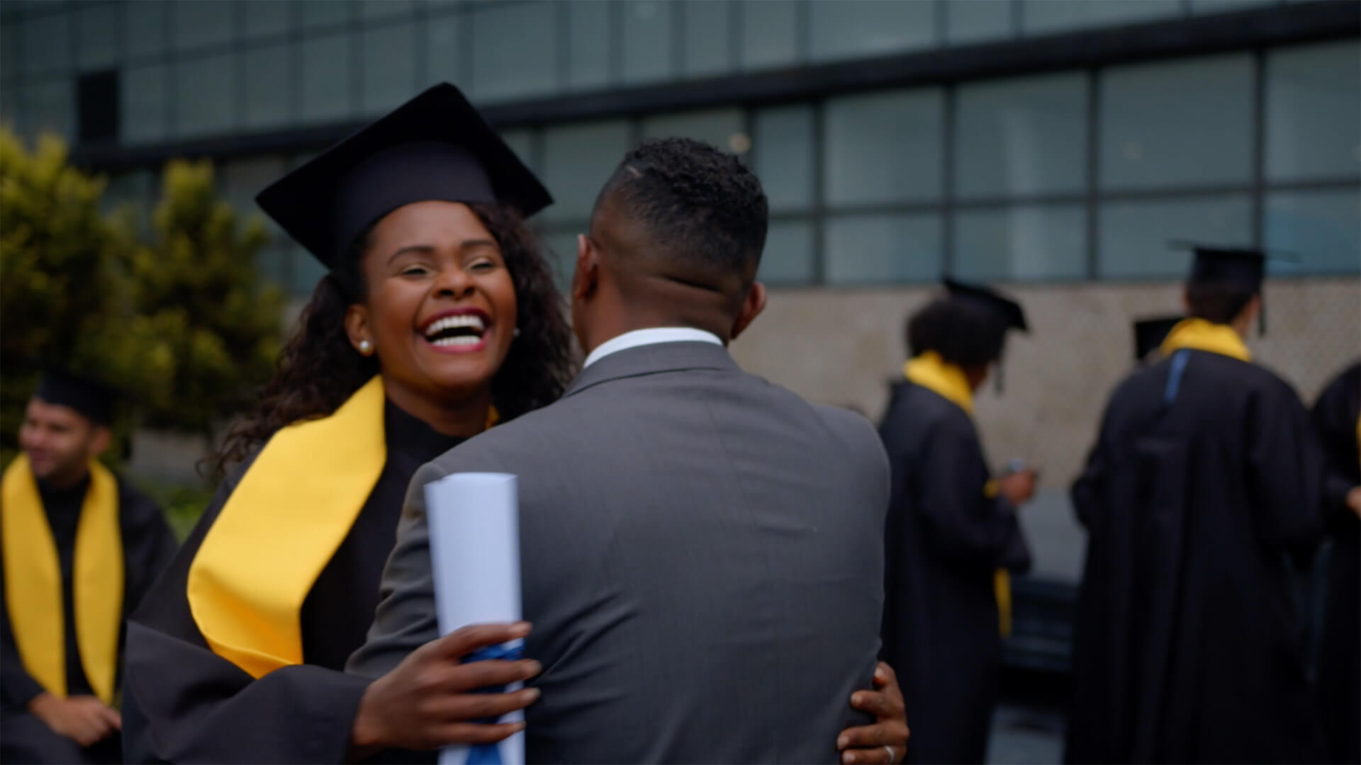 Enthused newly matriculated student with diploma hugs a Black college administrator.