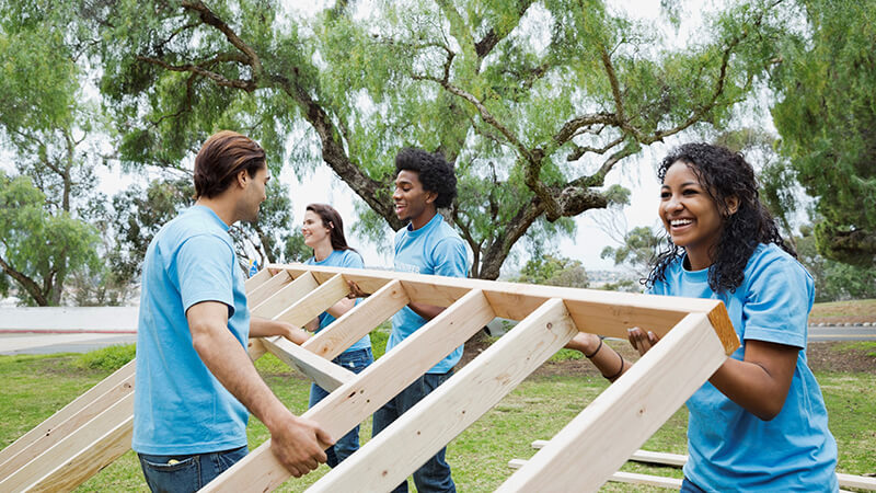 Happy volunteers lifting wooden frame together at park stock photo