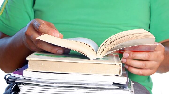 Student in green shirt with books in lap. Face not visible.