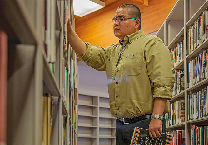 Native student in the stacks with a book.