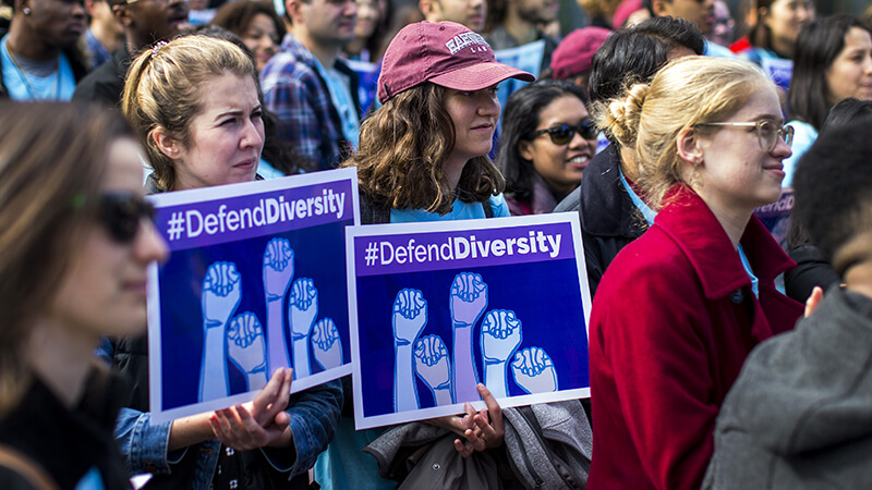 Tightly packed crowd of protesters outside the Supreme Court hold up signs reading Defend Diversity.